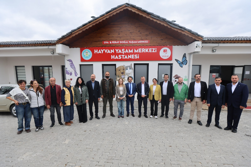 Oya & Feray Doğal Yaşam Merkezi ve Hayvan Yaşam Merkezi Hastanesi tabelasının bulunduğu tek katlı binanın önünde yan yana dizilmiş, resmi ve günlük kıyafetli bir grup insan poz veriyor. 