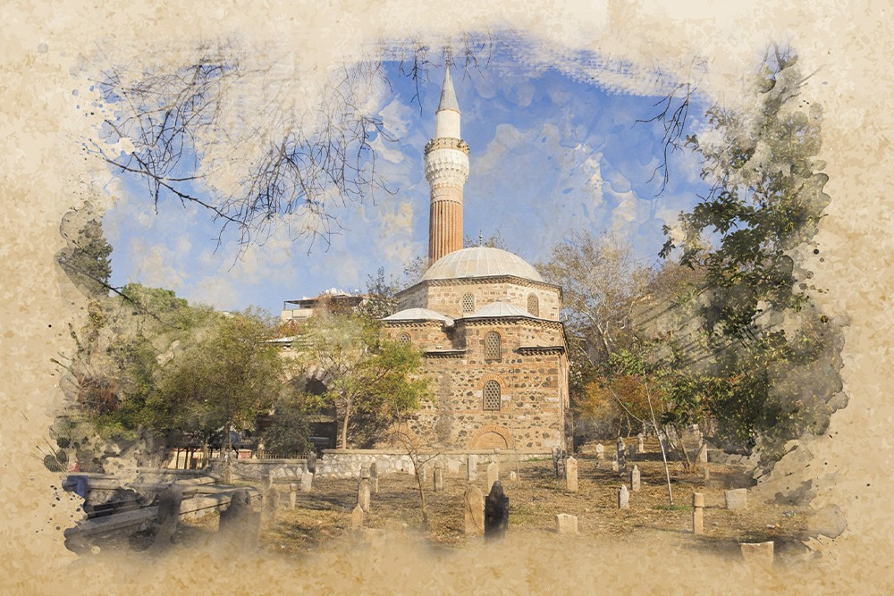 Taş duvarlı, tek minareli ve kubbeli tarihi bir cami ile önündeki eski mezar taşlarının bulunduğu bir bahçeyi gösteren, kenarları sulu boya efektiyle eskitilmiş bir manzara.